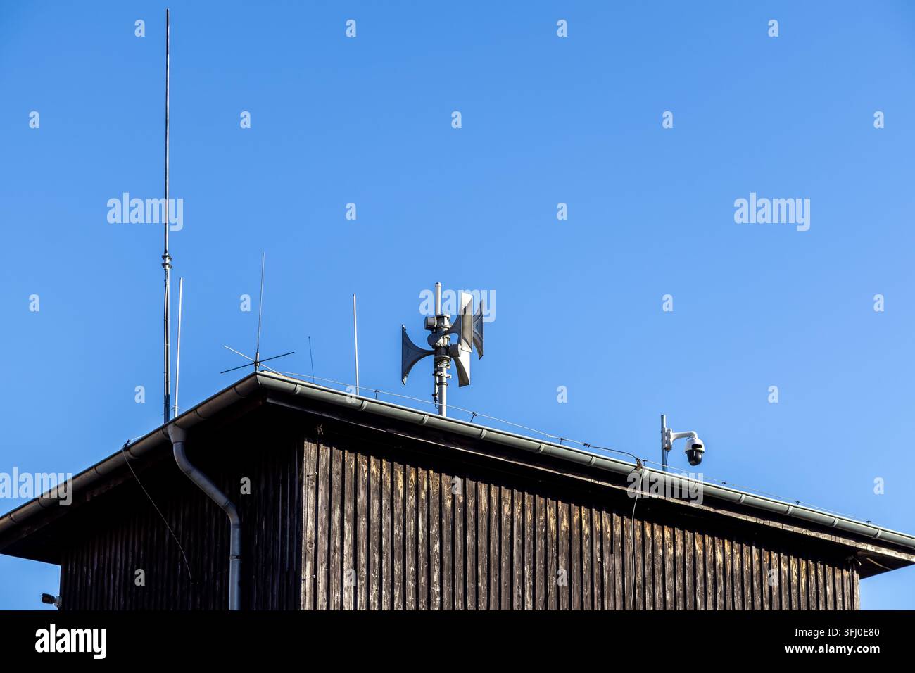 Una sirena di allarme pubblica e una telecamera di sicurezza montate su un tetto di legno rustico forniscono sicurezza, capacità di allarme e tecnologia di sorveglianza in un chiaro Foto Stock
