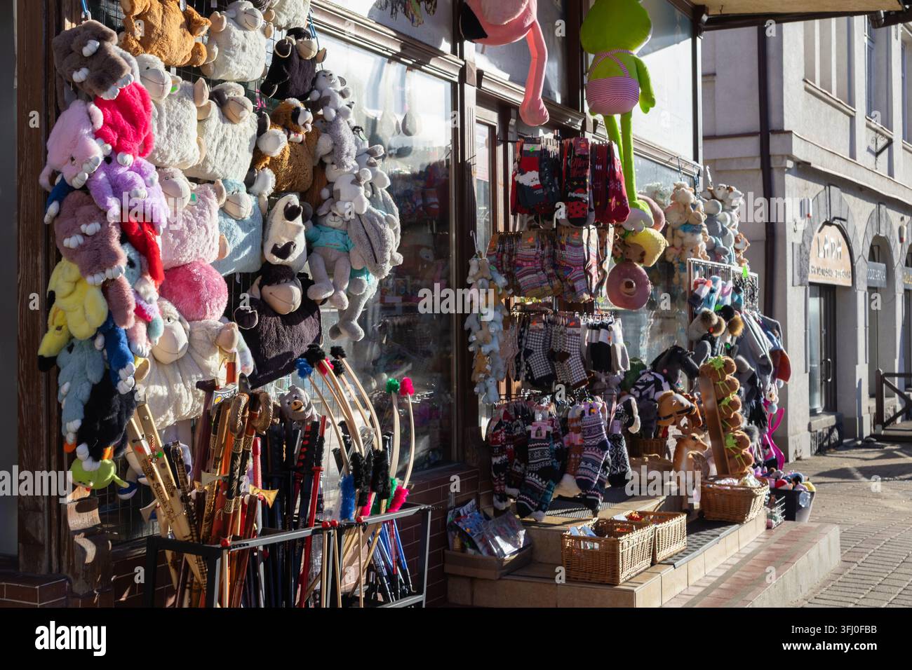 Szklarska Poręba, Polonia – 18 dicembre 2025: Bambole di peluche e accessori per bastoni intagliati sono disposti in vendita nella vetrina di un negoziante dove la giornata luminosa Foto Stock