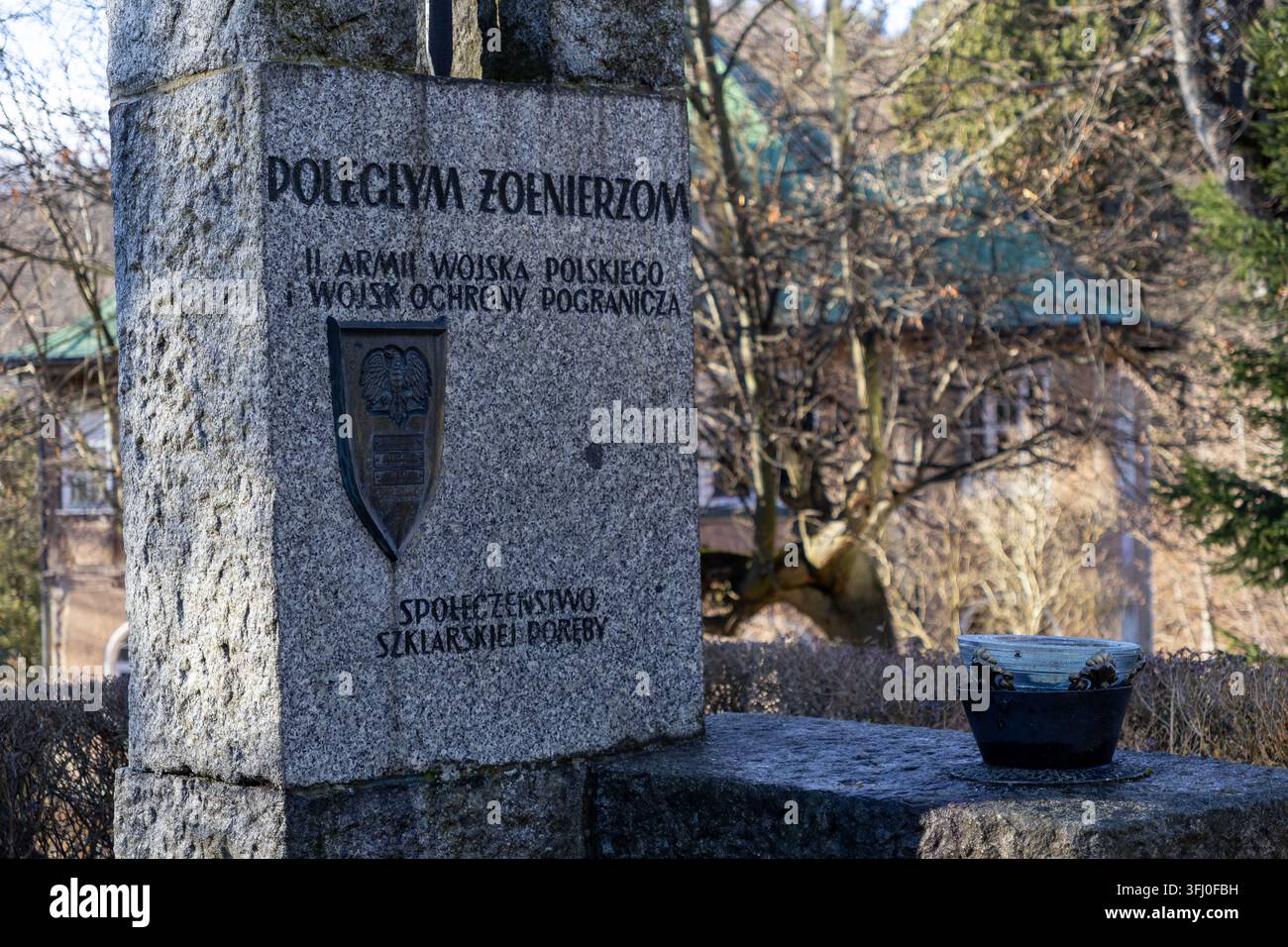 Szklarska Poręba, Polonia – 18 dicembre 2025: L’obelisco commemorativo in pietra onora i soldati caduti con testo inciso e un’insegna con aquila posizionata in un Foto Stock