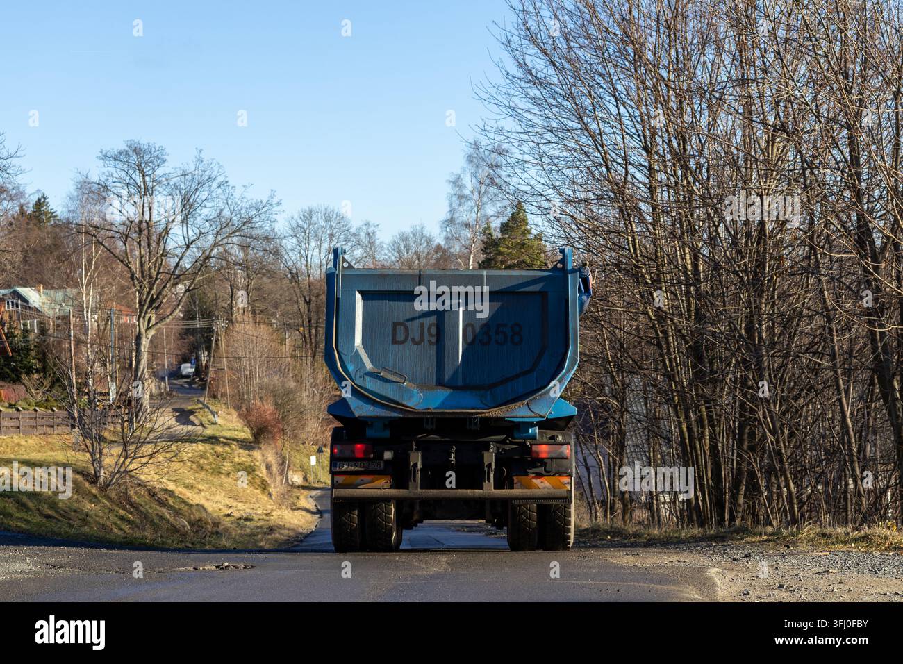 Szklarska Poręba, Polonia – 18 dicembre 2025: Grande veicolo blu a ribalta che percorre un sentiero di campagna tranquillo vicino a un’area boschiva, rappresentante il trasporto pesante Foto Stock