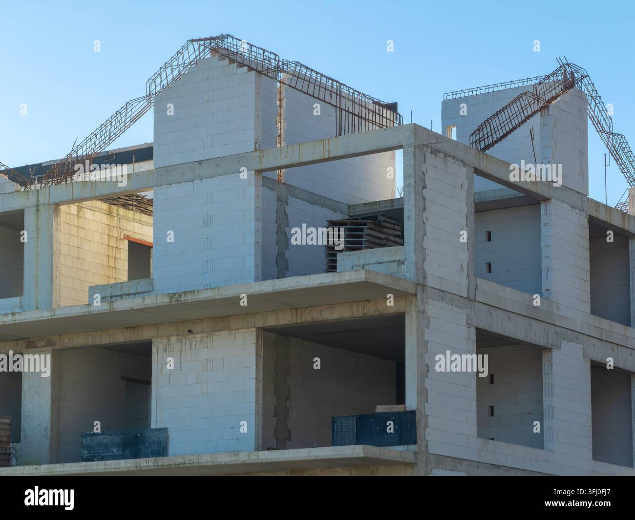 Struttura di palazzo residenziale a più piani in una fase iniziale di costruzione, con rinforzi in acciaio a vista e blocchi cavi che rappresentano la crescita industriale e Foto Stock