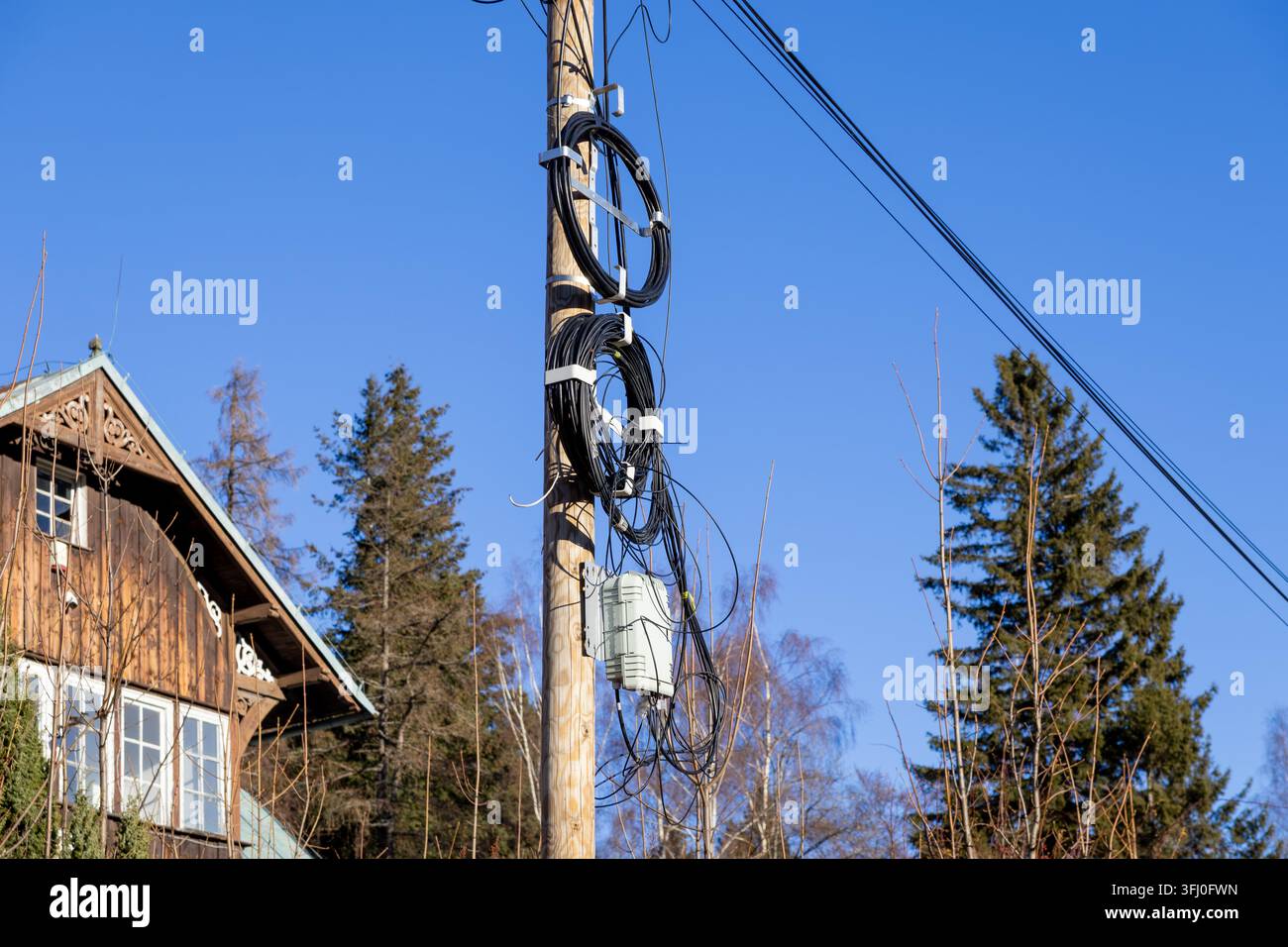Attrezzature di distribuzione in fibra ottica montate su un palo di legno accanto a una casa residenziale, che mostrano un'infrastruttura di connettività di rete moderna integrata Foto Stock
