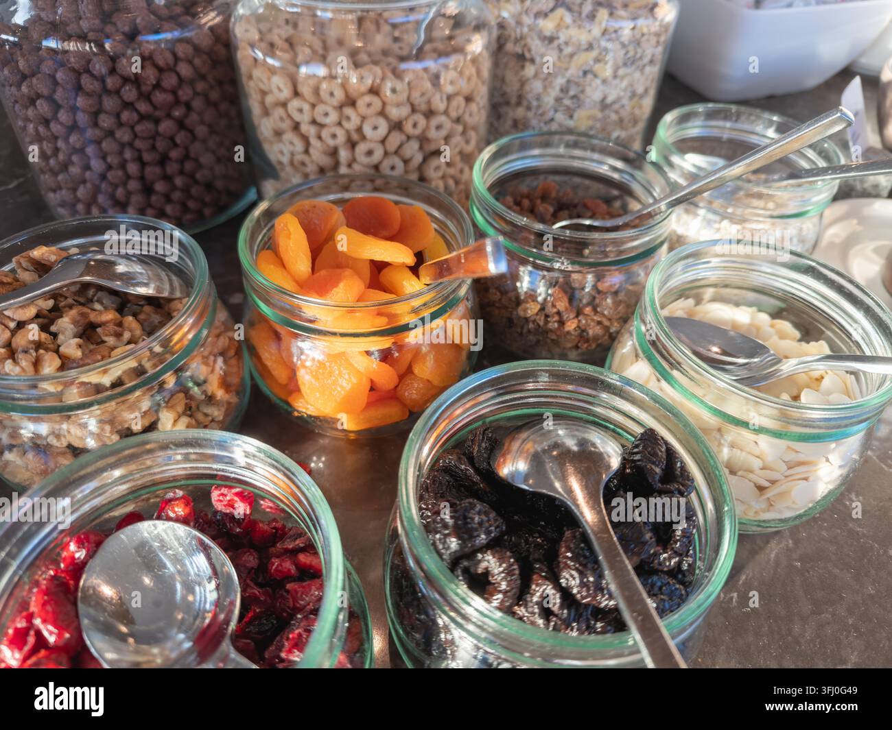 Contenitori di vetro ripieni di noci, albicocche secche, uvetta, prugne e scaglie di mandorle, disposti per un'offerta organizzata per la colazione mattutina Foto Stock