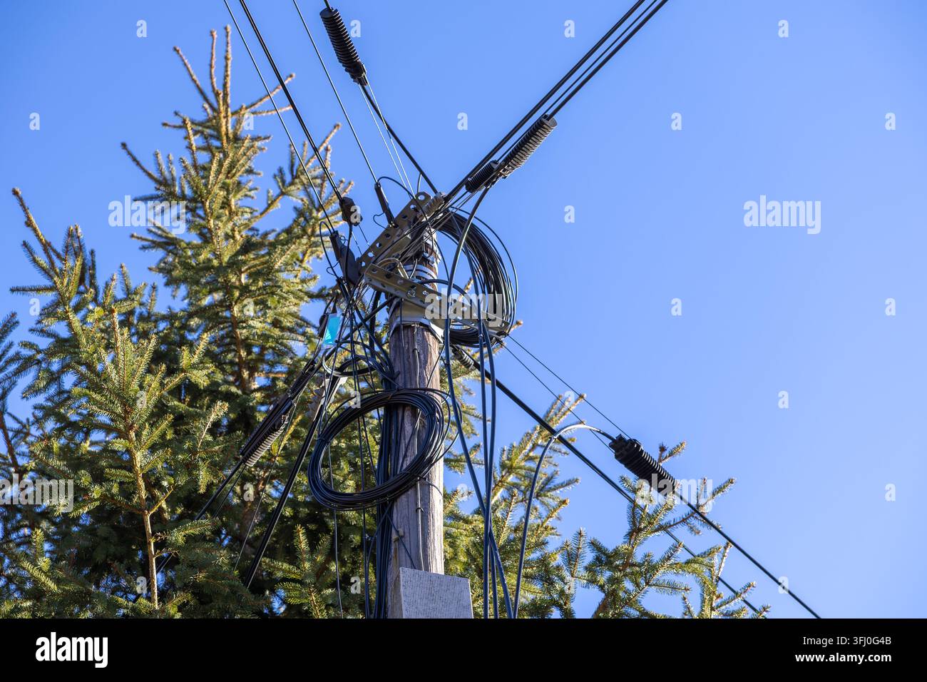 Un palo elettrico invecchiato porta una fitta rete di fibre ottiche e cavi raggruppati, rappresentando la complessità della rete moderna, l'infrastruttura di comunicazione digitale Foto Stock