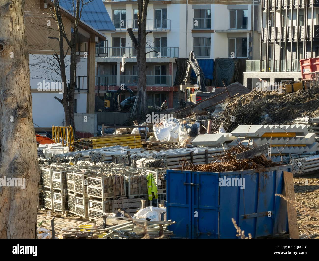 Szklarska Poręba, Polonia – 18 dicembre 2025: pile di impalcature, macchine pesanti e bidoni per rifiuti metallici occupano un cantiere edile vicino a uno moderno Foto Stock