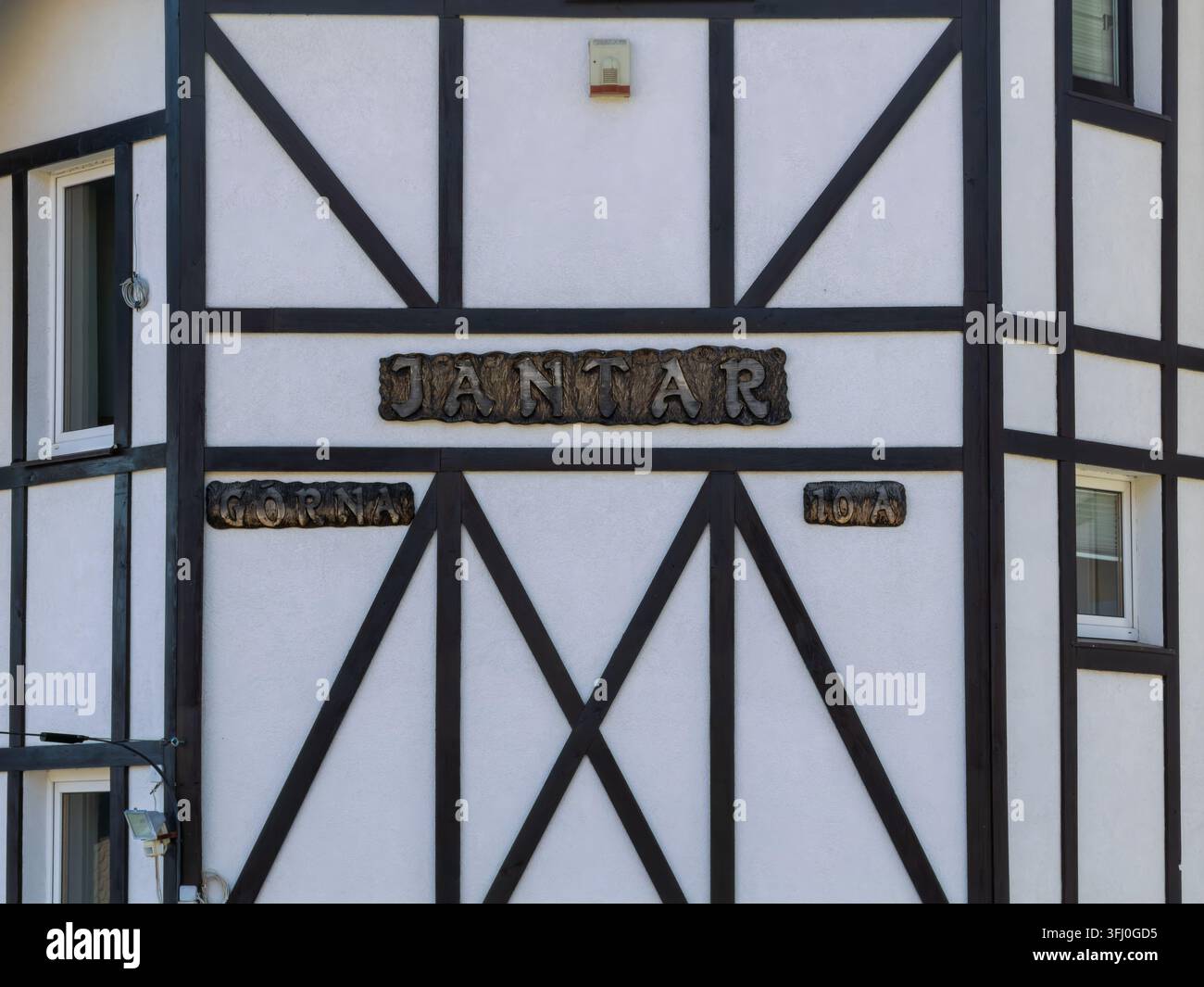 Szklarska Poręba, Polonia – 18 dicembre 2025: Parete bianca di un edificio con telai in legno nero ed etichette in legno rustico, che rappresentano l’artigianato storico Foto Stock