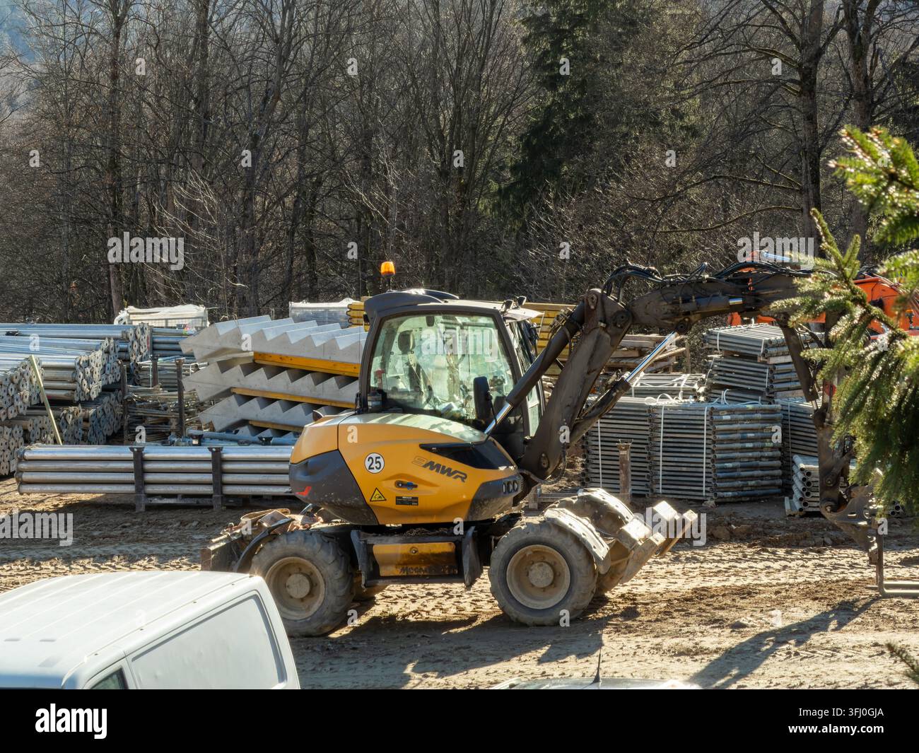 Szklarska Poręba, Polonia – 18 dicembre 2025: Escavatore su ruote Mecalac in piedi vicino a materiali da costruzione industriali e pile di impalcature durante un ca Foto Stock