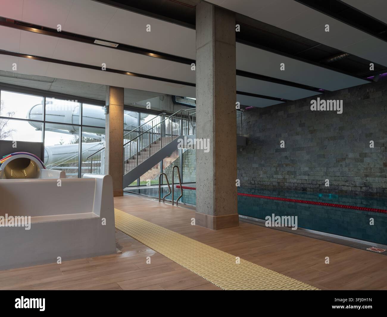 La struttura ricreativa contemporanea include una piscina limpida e una scala luminosa che porta all'esterno, creando un'atmosfera tranquilla per il relax e il fitness Foto Stock