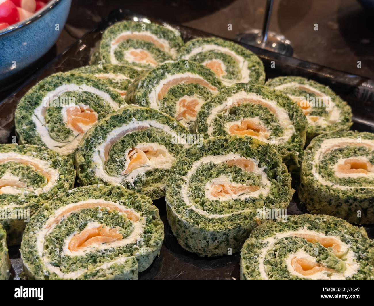 Pezzi di involtini di verdure verdi appetitosi con formaggio cremoso e fette di pesce arancioni disposti su un piatto da portata, evidenziando uno spuntino culinario sano Foto Stock