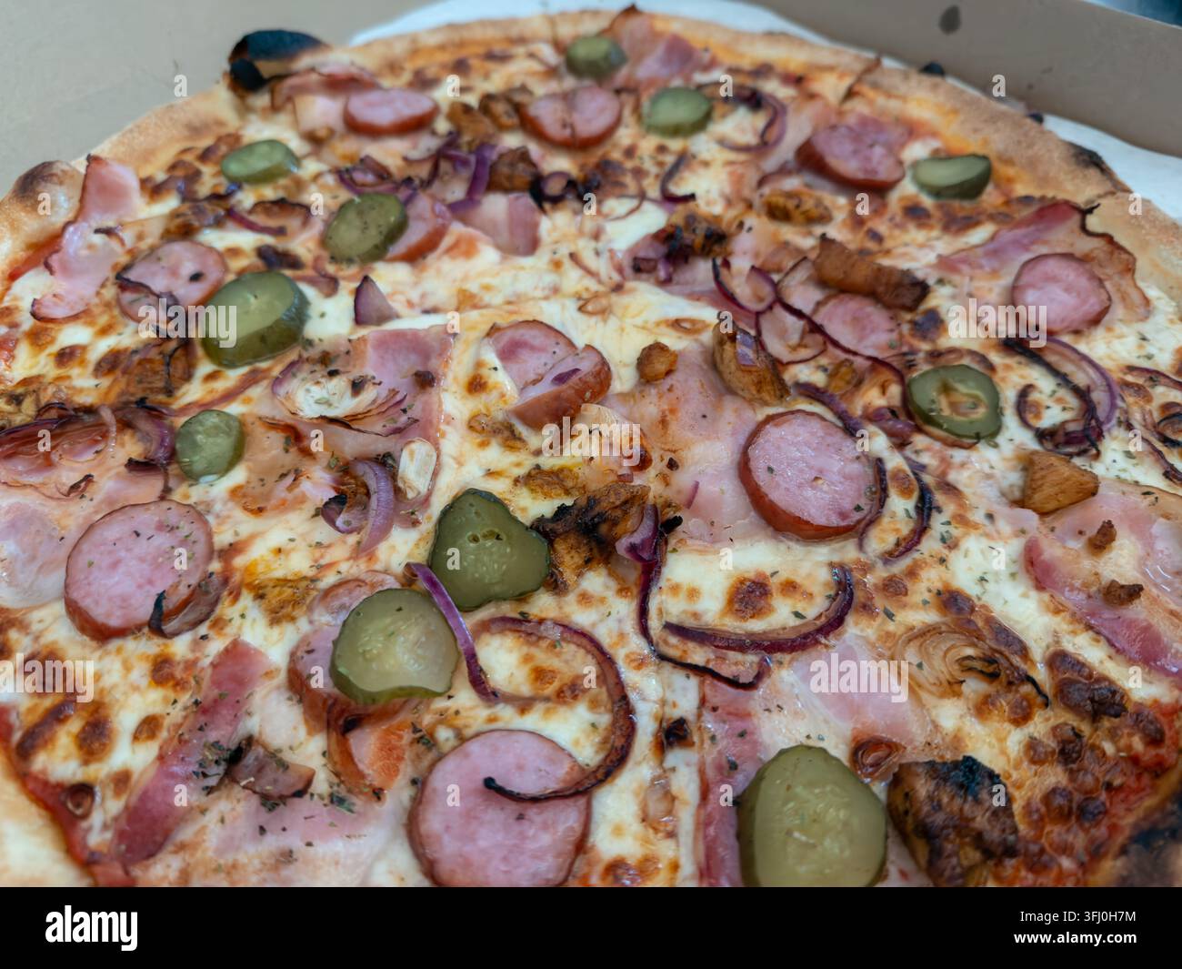 Una crosta di pizza appetitosa presenta strati di formaggio fuso, carne stagionata, fette di cipolla e sottaceti piccanti, catturando perfettamente un delizioso piatto da asporto Foto Stock