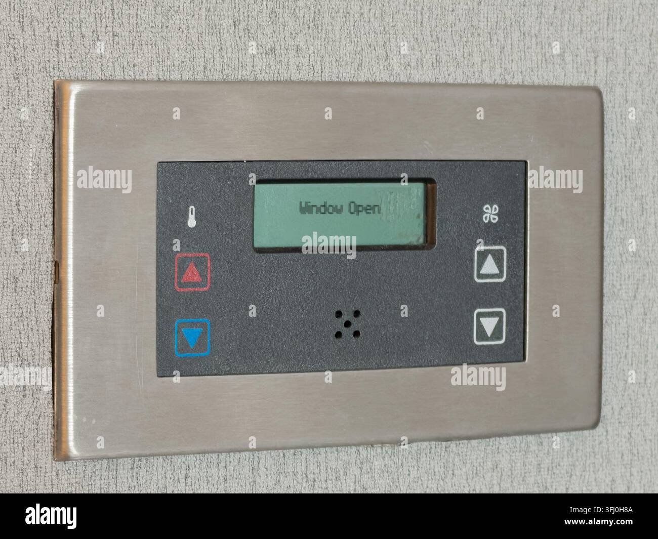 Il regolatore climatico in acciaio inossidabile montato su un muro grigio mostra un avviso di finestra aperta, indicando il monitoraggio attivo della temperatura dell'aria interna Foto Stock