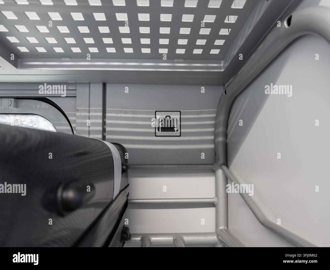 Il bagaglio rigido è posizionato in modo sicuro su una mensola portabagagli in acciaio contemporanea sopra i sedili dei passeggeri in un treno, illustrando un'organizzazione efficiente dei viaggi Foto Stock