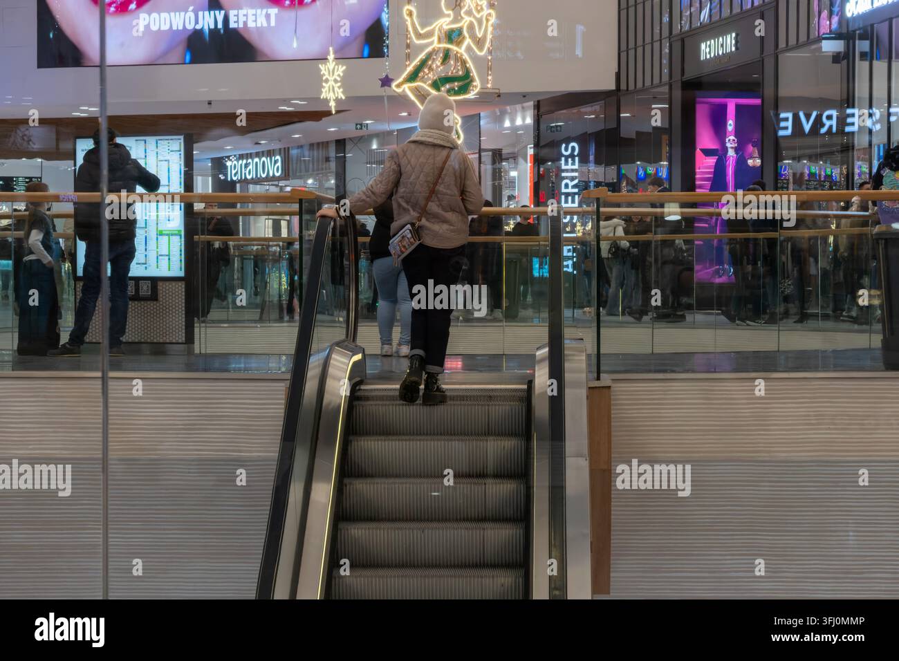 Wroclaw, Polonia – 9 dicembre 2025: Gli acquirenti camminano vicino ai gradini delle scale mobili in un centro commerciale interno luminosissimo, rappresentando un'atmosfera festiva Foto Stock
