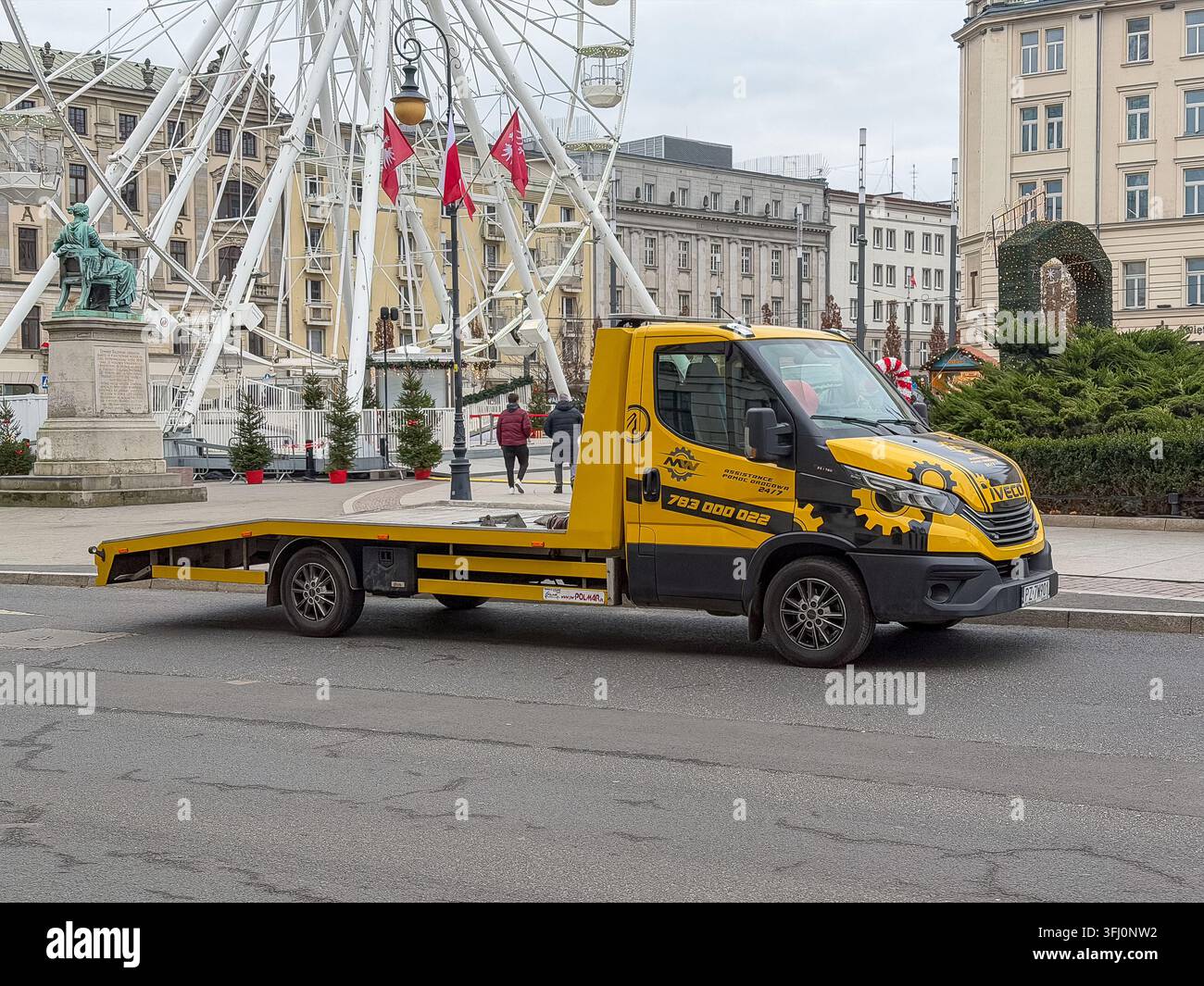 Poznań, Polonia - 23 dicembre 2025: Un veicolo di soccorso Iveco si trova su una piazza cittadina vicino a un punto di riferimento, illustrando un aiuto professionale in caso di guasto e em Foto Stock