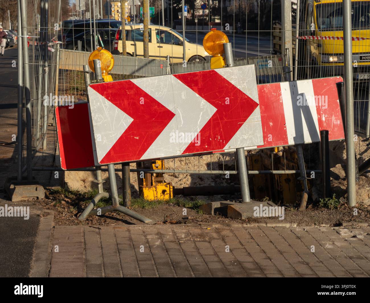 I segnali a forma di freccia rossi e bianchi indicano una deviazione per i veicoli vicino a uno scavo delle utility cittadine, evidenziando lo sviluppo urbano, i progetti di manutenzione e Foto Stock