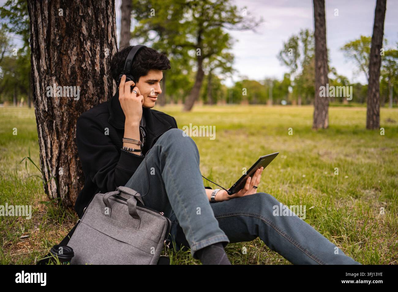 Studente giovane adulto che impara con tablet e cuffie all'aperto Foto Stock