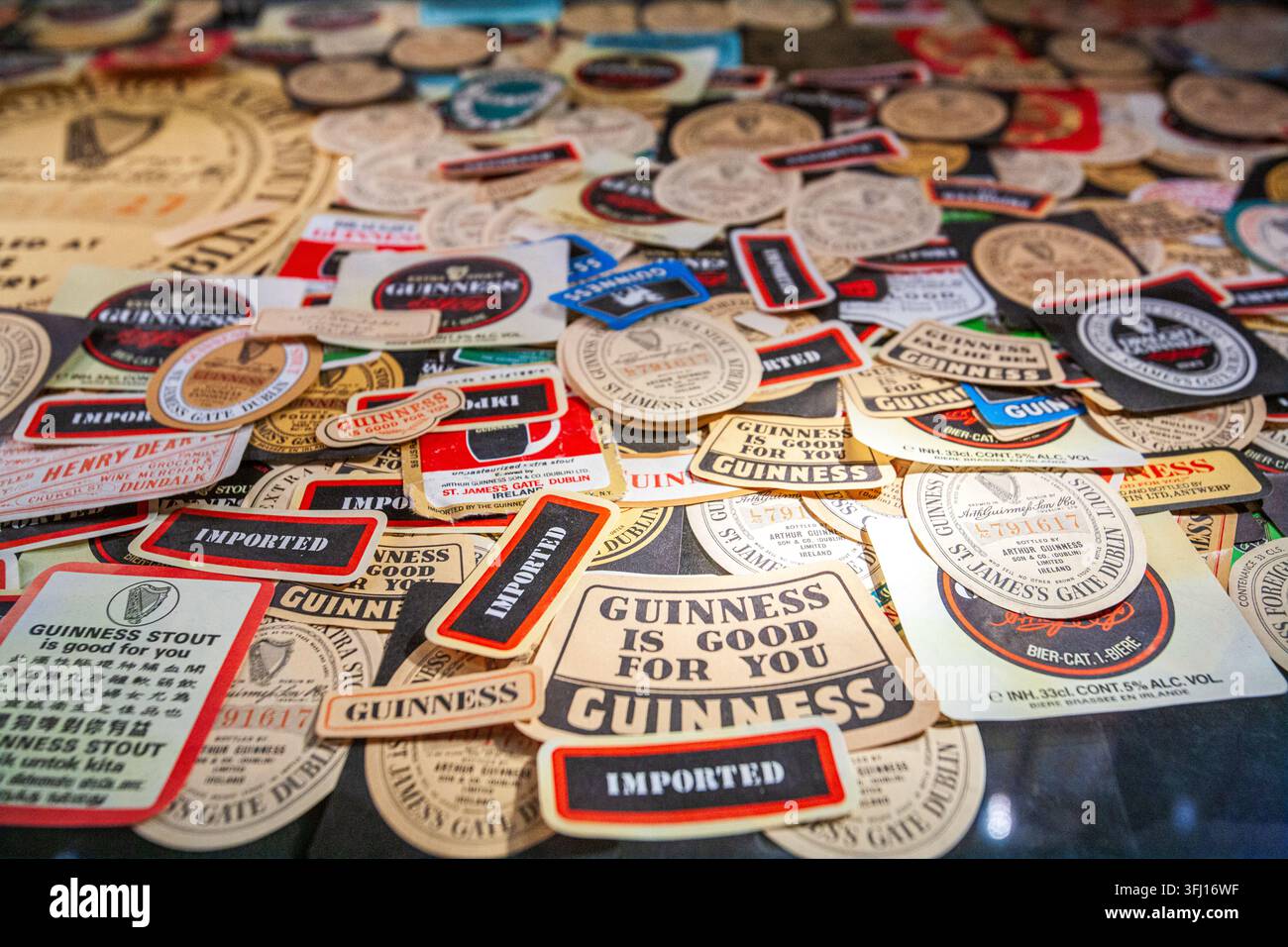 Una vivace esposizione di etichette e sottobicchieri di birra Guinness internazionali diversificati, che mostrano la storia globale del marchio. Fotografato al Guinness Stor Foto Stock
