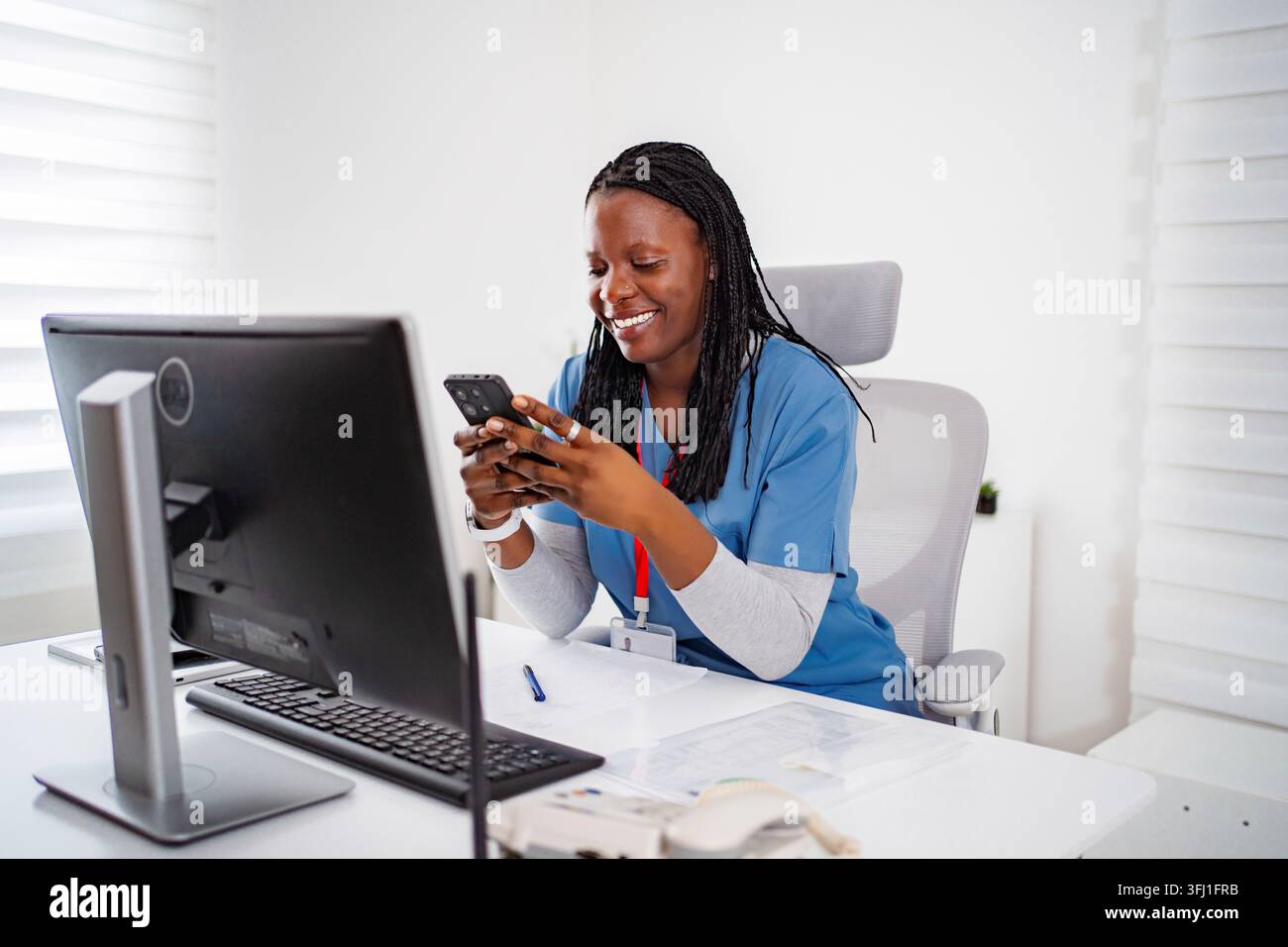 Infermiera sorridente che usa uno smartphone in una clinica d'ufficio Foto Stock