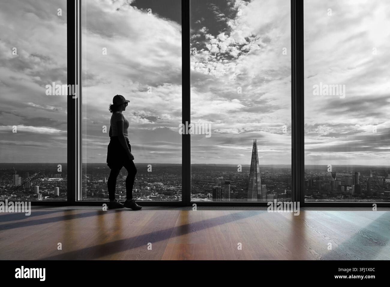 Silhouette di una donna che guarda fuori da una finestra a tutta altezza sulla skyline di Londra con vista su The Shard dal 50° piano di The Lookout, 8 Bishopsgate Foto Stock