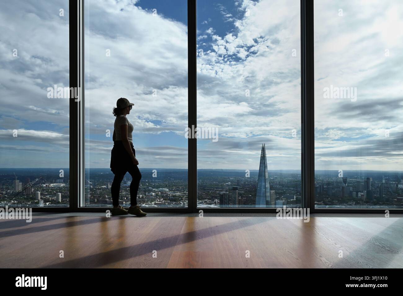 Silhouette di una donna che guarda fuori da una finestra a tutta altezza sulla skyline di Londra con vista su The Shard dal 50° piano di The Lookout, 8 Bishopsgate Foto Stock