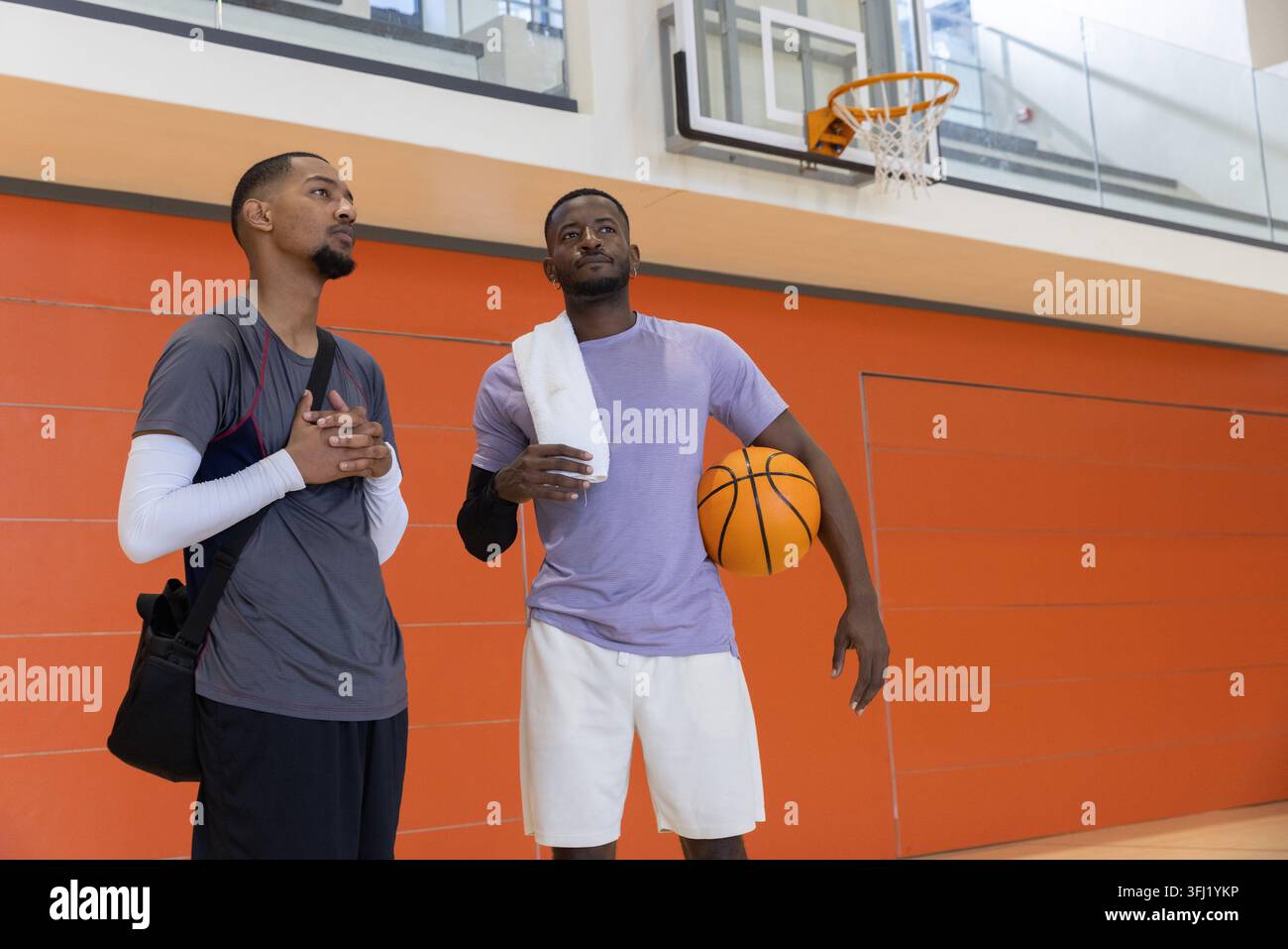 Diversi amici maschi che chiacchierano sul campo da basket in palestra con attrezzatura sportiva che tiene la palla vicino al cerchio. Atletica, cameratismo, conversazione, struttura, vibrante, o Foto Stock