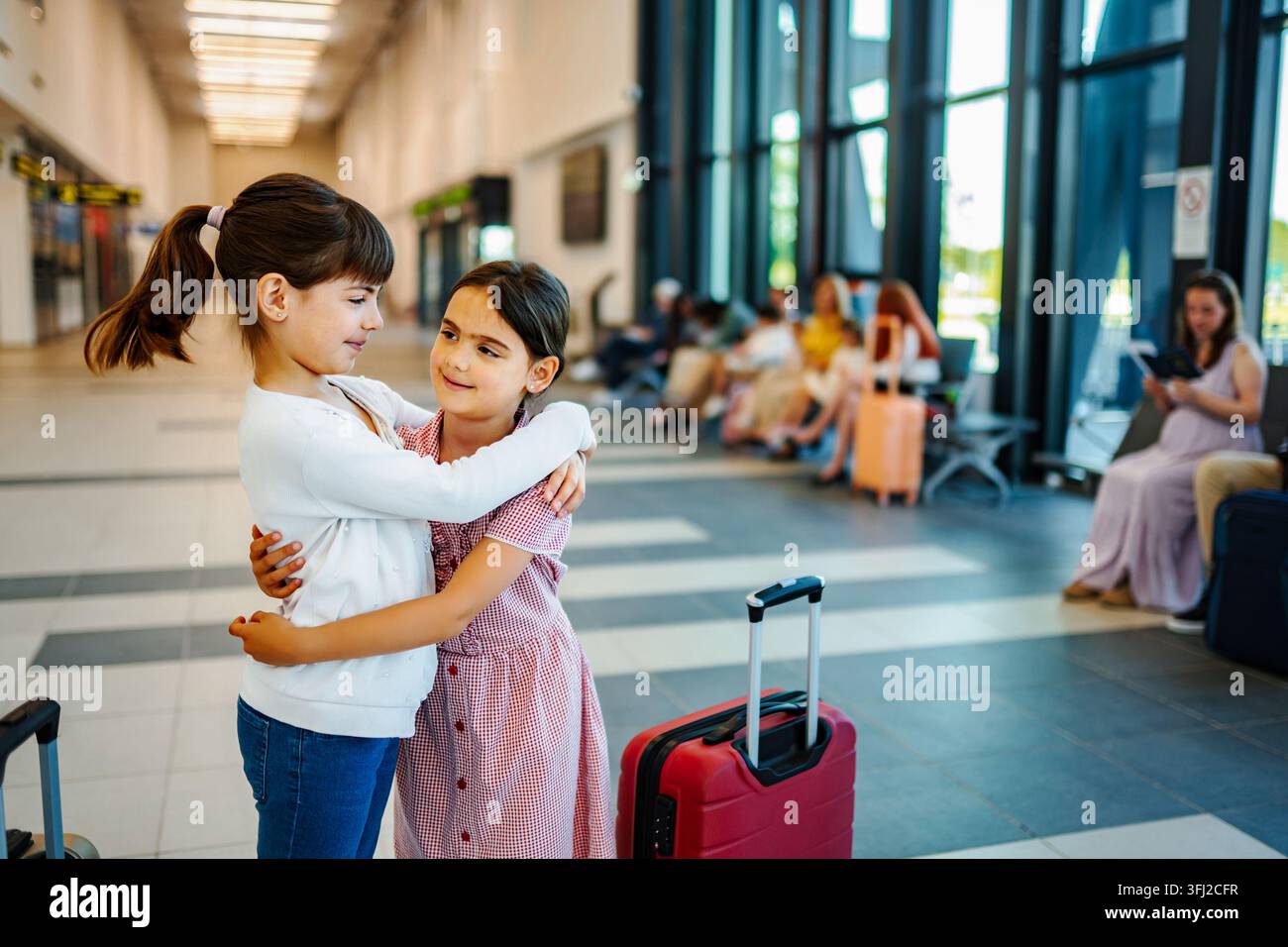 Due ragazze che si abbracciano nella sala d'attesa dell'aeroporto con una valigia Foto Stock
