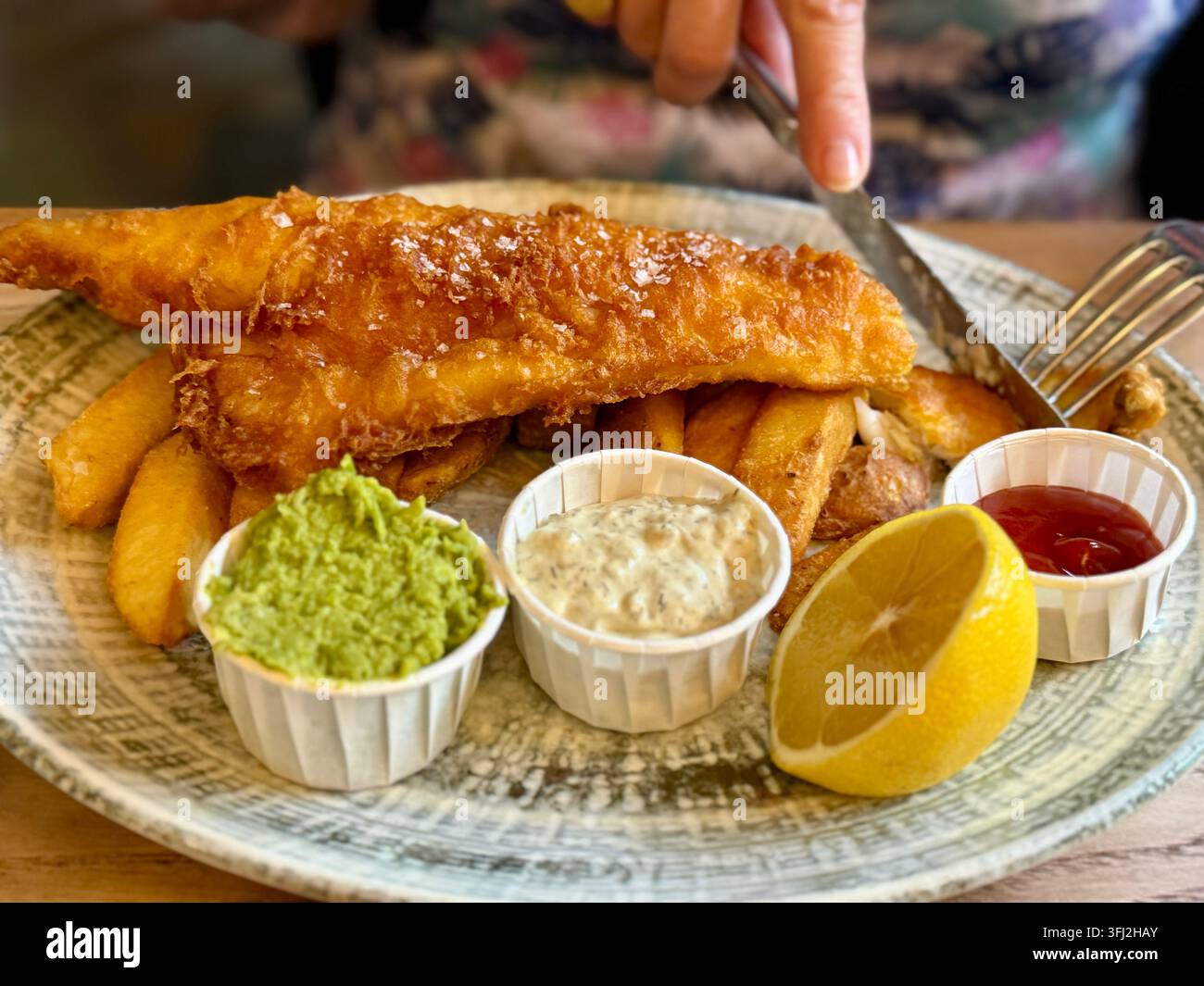 Prima piano di una donna che mangia un piatto di fish and chips con piselli schiacciati, salsa tartara e ketchup Foto Stock