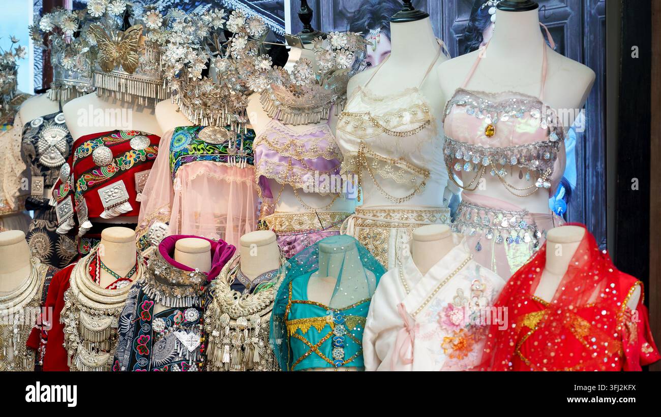 Costumi etnici colorati in stile tradizionale e copricapi d'argento esposti in un negozio nella vecchia città di Lijiang, Yunnan, Cina Foto Stock