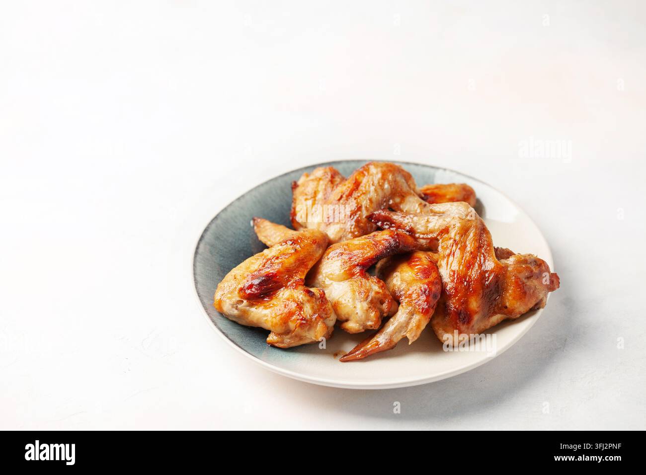 Le ali di pollo grigliano in un piatto su uno sfondo luminoso. Foto Stock