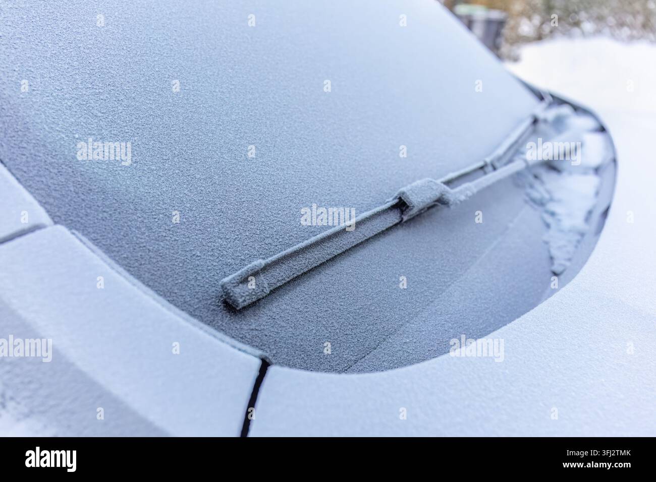 La priorità della pulizia del parabrezza si concentra su un tergicristallo ricoperto di brina appoggiato su un vetro automobilistico opaco, mostrando la necessità pratica di rimuovere il ghiaccio prima Foto Stock