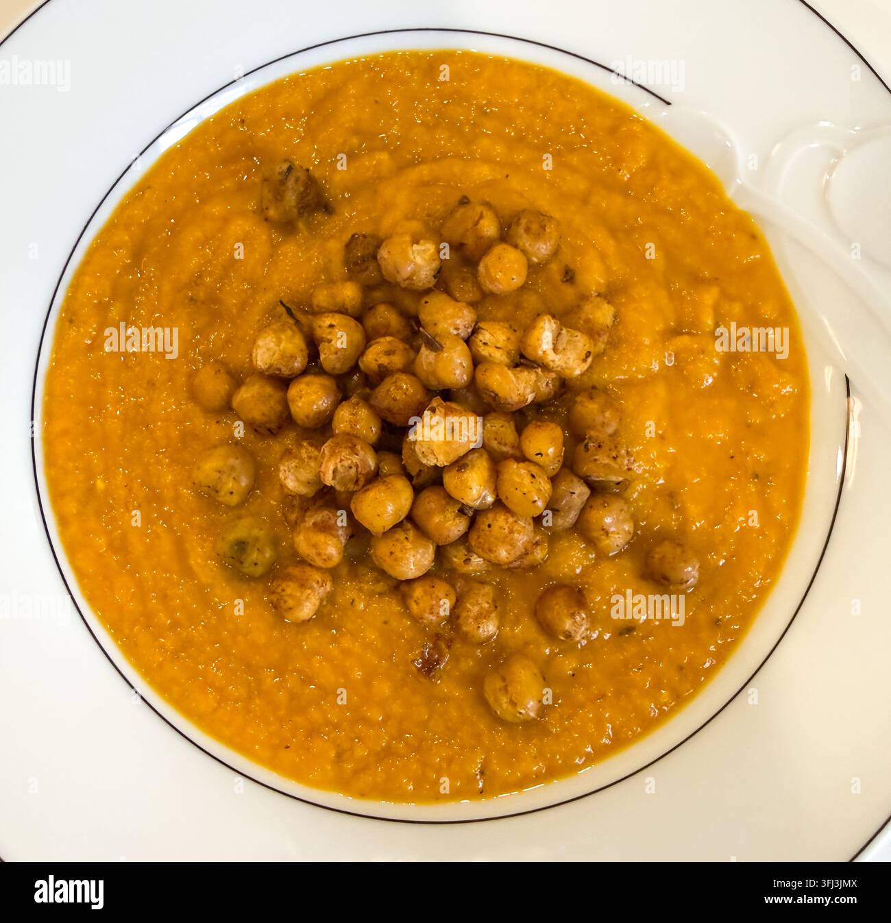 Prima vista di una ciotola di zuppa di carote sormontata da ceci croccanti e speziati. Foto Stock
