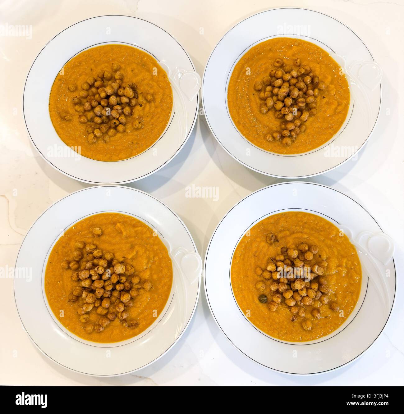 Quattro ciotole di zuppa di carote ricoperte di ceci croccanti e speziati. Foto Stock