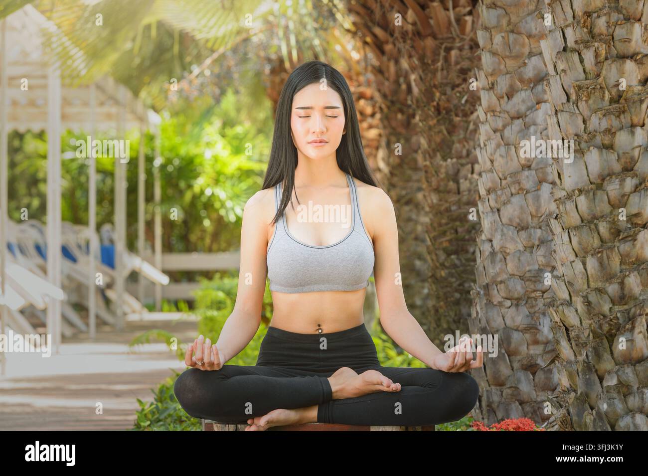 Giovane donna in abbigliamento sportivo seduta all'aperto in una posizione di loto incrociato (Padmasana) con gli occhi chiusi e le mani in una posizione mudra del mento, che pratica la meditazione consapevole Foto Stock