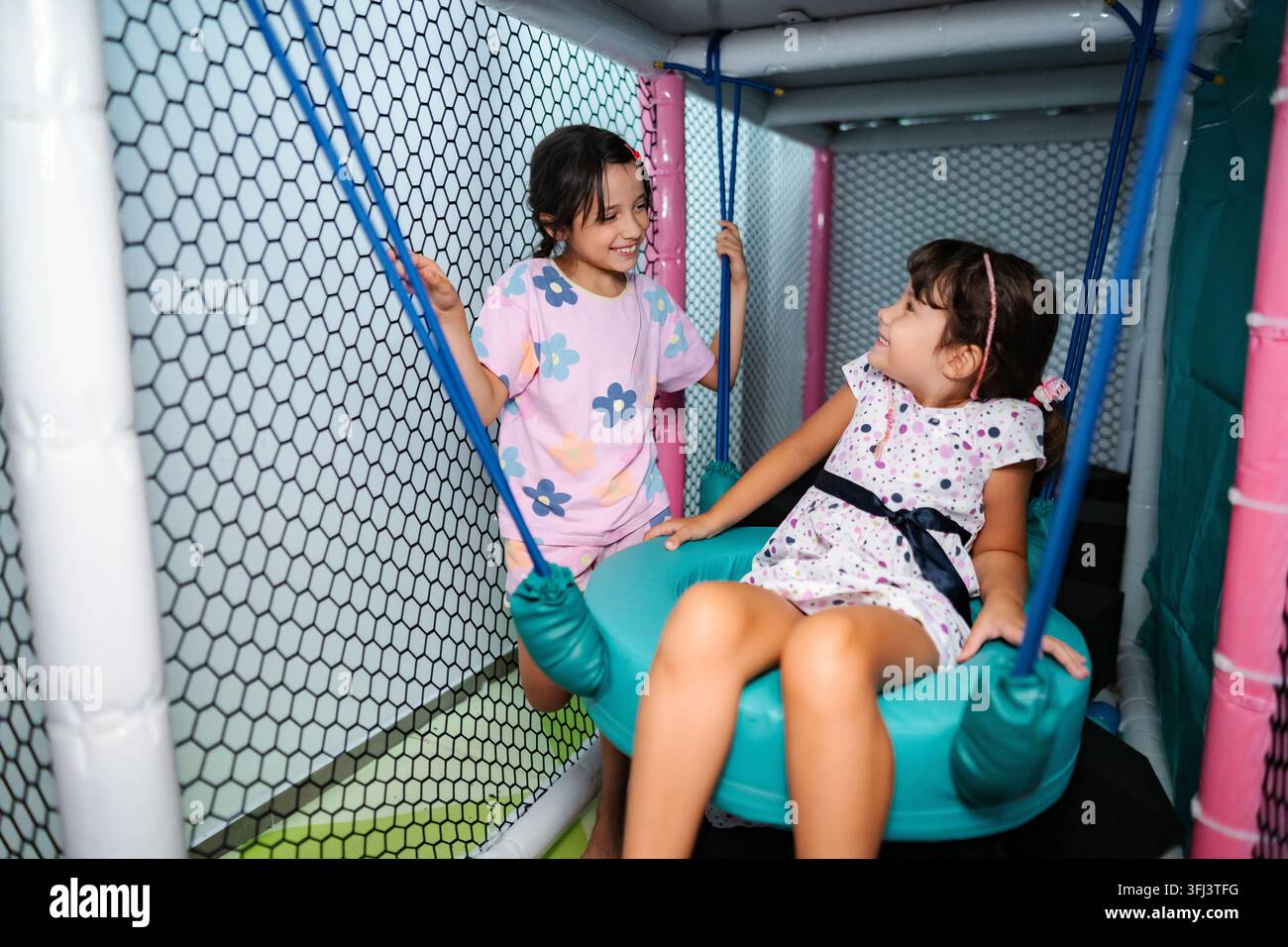 Ragazze felici che giocano sull'altalena divertendosi in un parco giochi al coperto Foto Stock