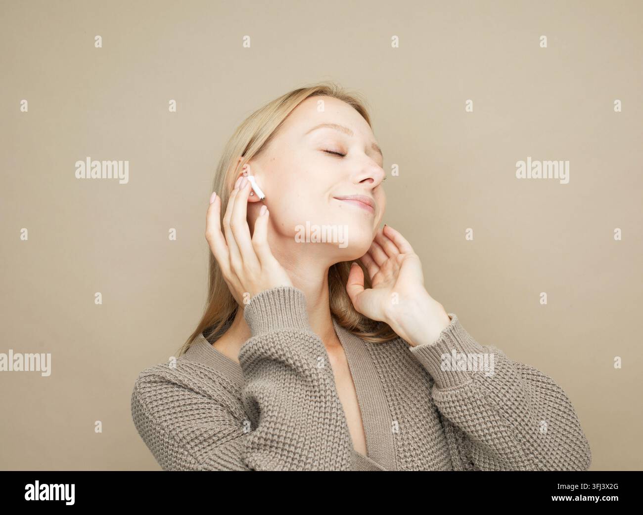 Bella giovane donna bionda con cuffie che ascolta musica su sfondo beige. Foto Stock