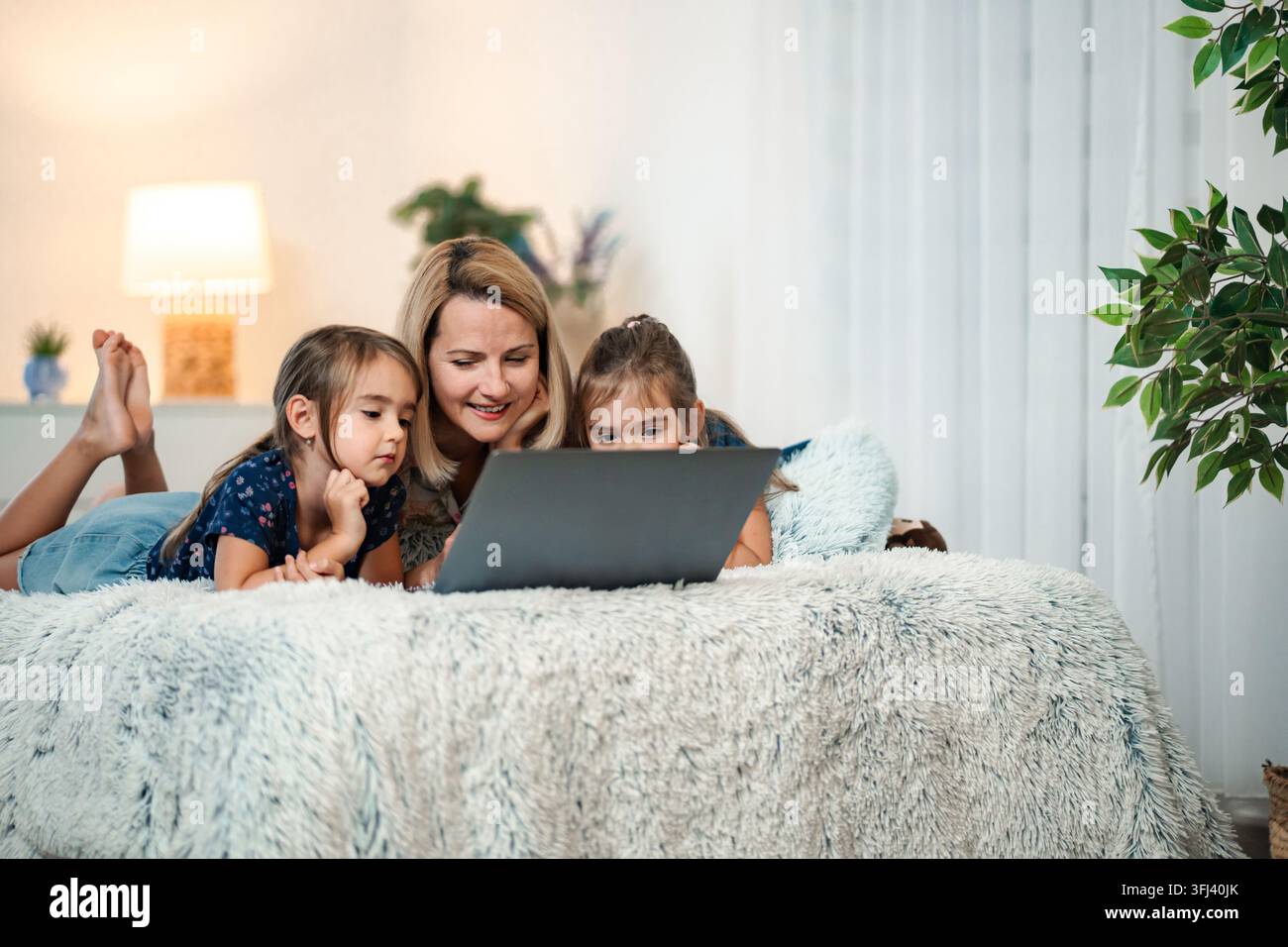 Madre e figlie gemelle che guardano insieme un laptop sul letto Foto Stock