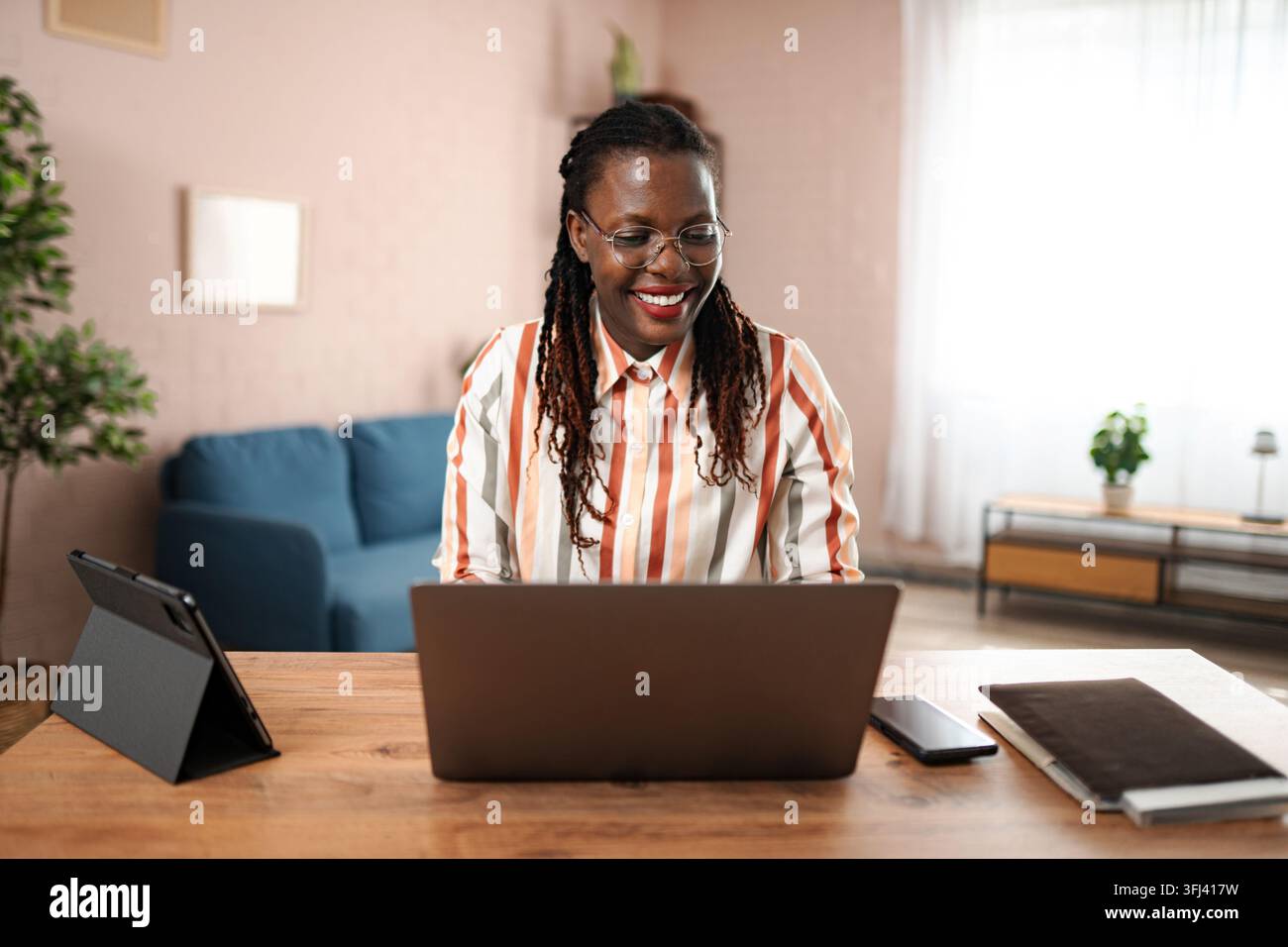 Donna afroamericana che sorride mentre lavora da casa Foto Stock