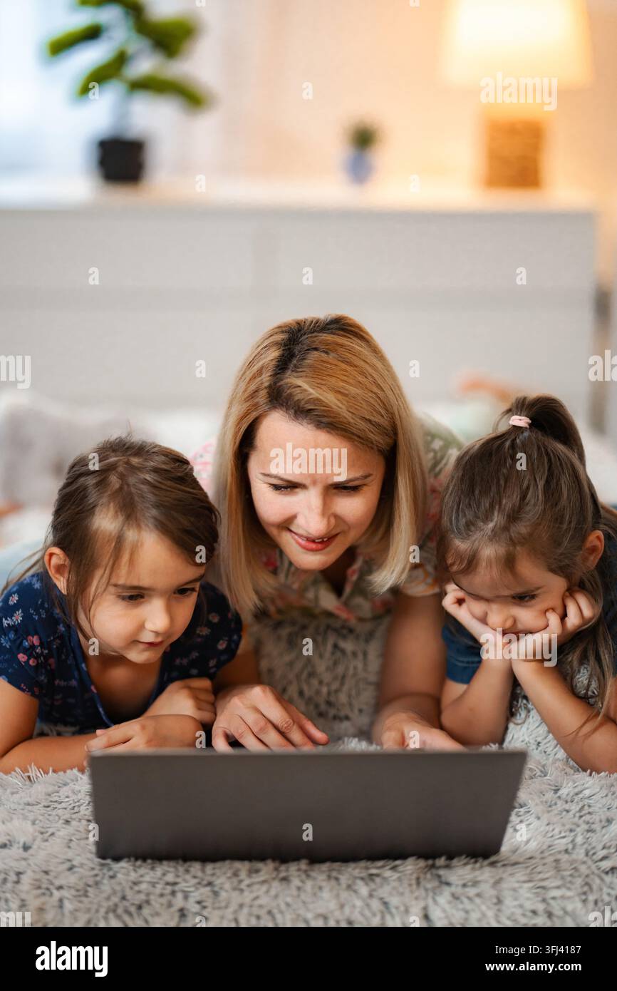 Madre e due bambine che imparano insieme utilizzando un laptop a casa Foto Stock