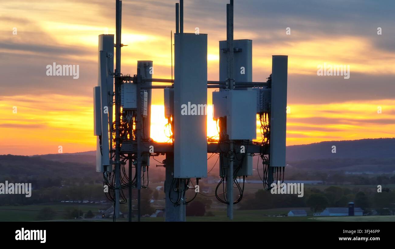 Torre di telefonia cellulare durante un tramonto arancione. Orbita aerea con zoom lungo. Tema di connettività e servizio cellulare nelle zone rurali degli USA, Ephrata, Pennsylvania. Foto Stock