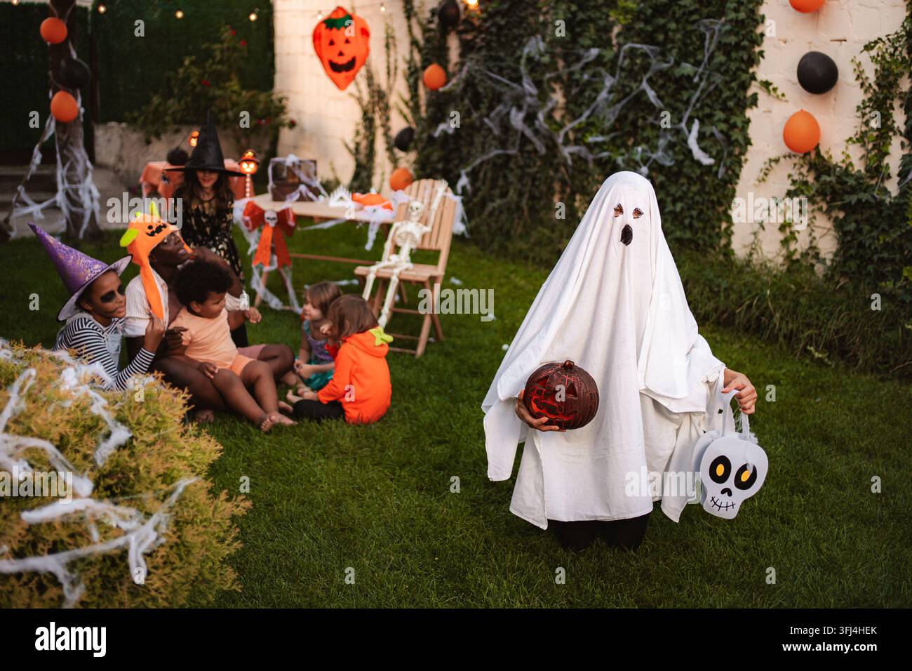 Bambino in costume da fantasma con zucca e secchio di dolcetti Foto Stock