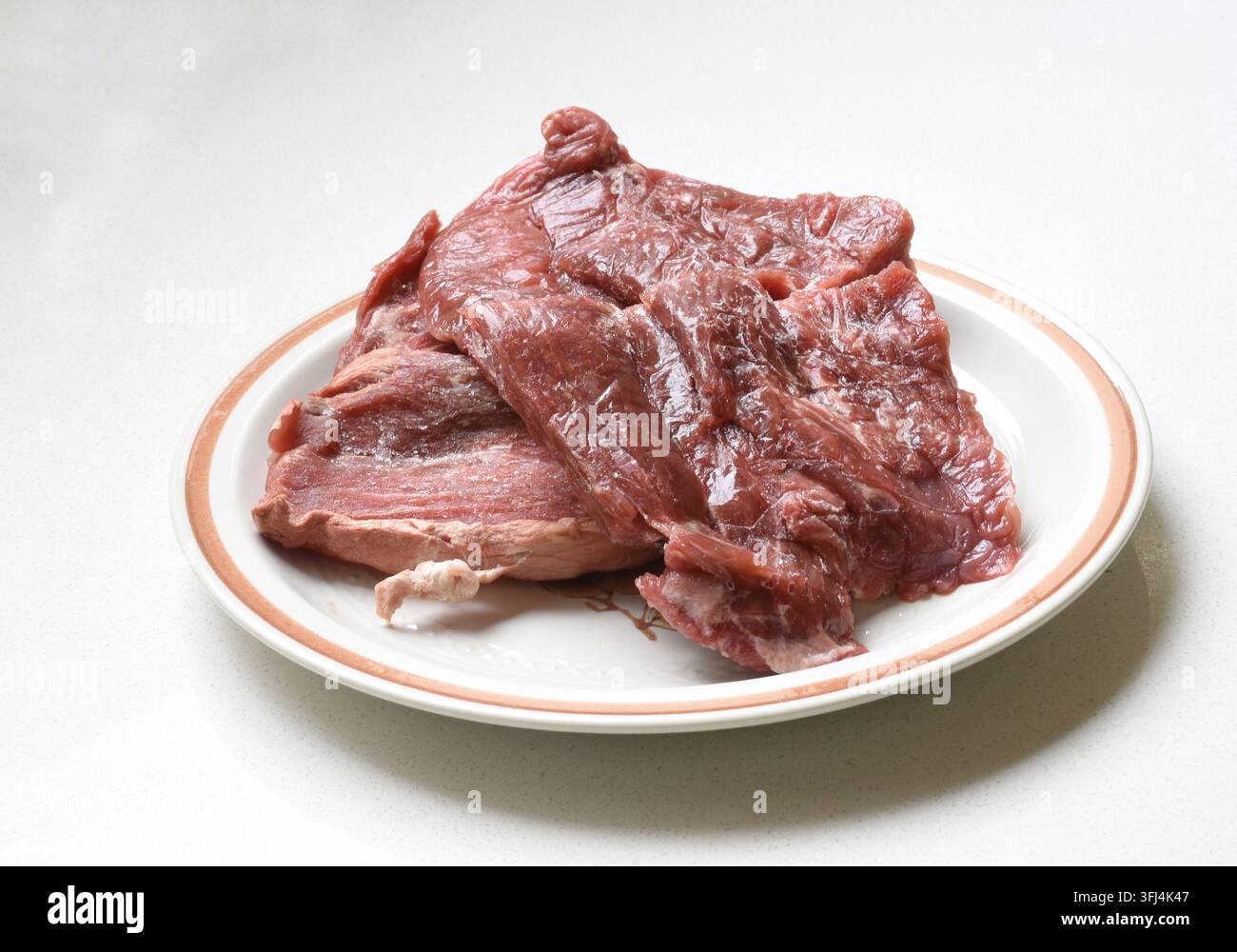 Carne rossa cruda fresca disposta su un piatto su un tavolo di legno, evidenziando la texture naturale, il colore e la preparazione del cibo. Foto Stock