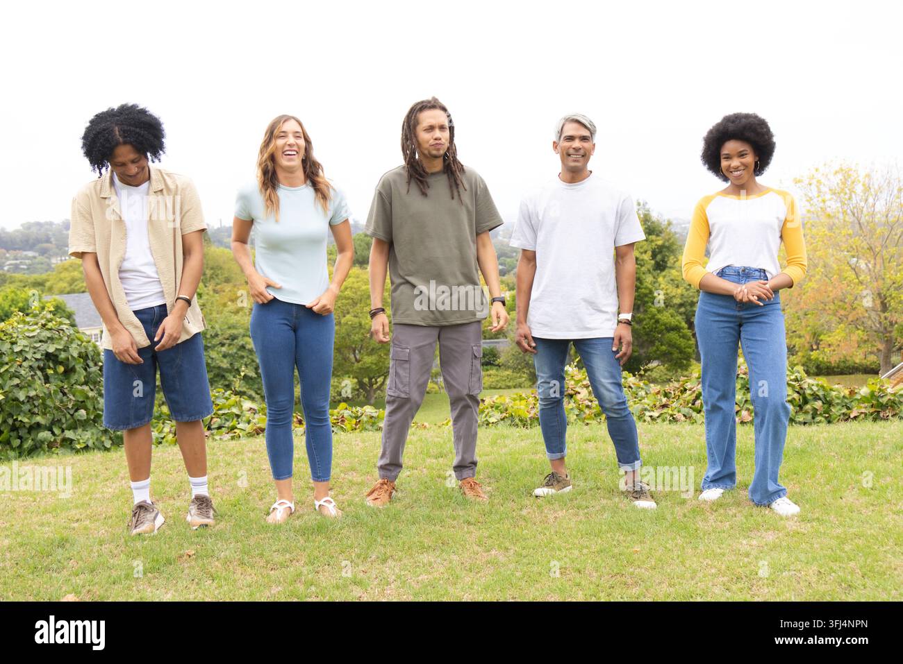 Amici diversi in piedi fianco a fianco su un pendio erboso in un parco suburbano, indossano abiti casual. All'aperto, gruppo, cinque, adulti, i Foto Stock