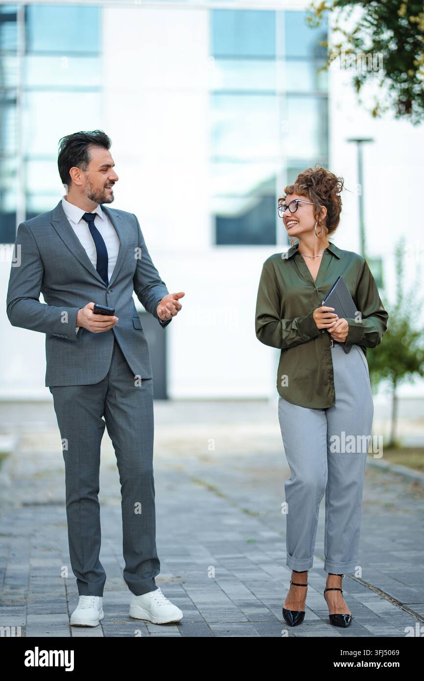 Persone d'affari che conversano camminando all'aperto con un edificio Foto Stock