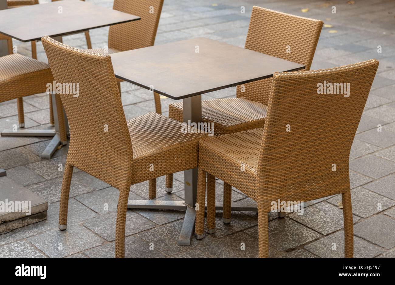 Sedere di vimini vuoti circondano tavoli quadrati su una terrazza esterna lastricata. Foto Stock