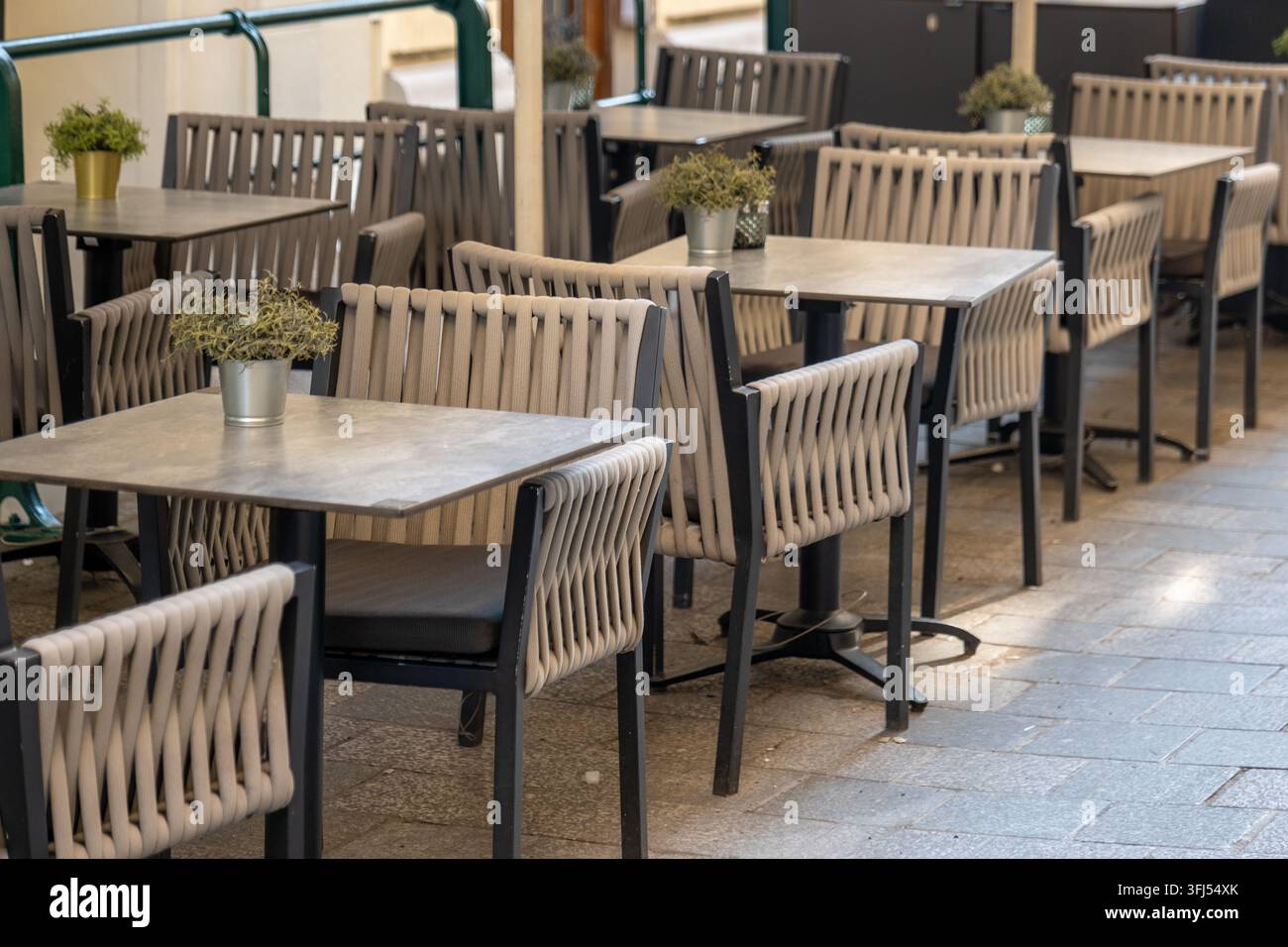 Terrazza di caffè moderna vuota con sedie intrecciate, tavoli quadrati e piccole piante in vaso. Foto Stock