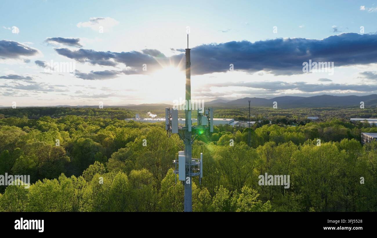 Tramonto dorato in un paesaggio boschivo lussureggiante con torre di telecomunicazioni in un sobborgo americano. Ripresa aerea orbitante. Tema 4G e 5G, Lynchburg, Virginia. Foto Stock