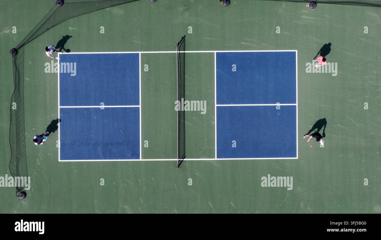 Gioco tradizionale di pickleball con due squadre di giocatori su un campo all'aperto sotto il sole splendente, che mostra attività sportiva ricreativa, lavoro di squadra e salute Foto Stock