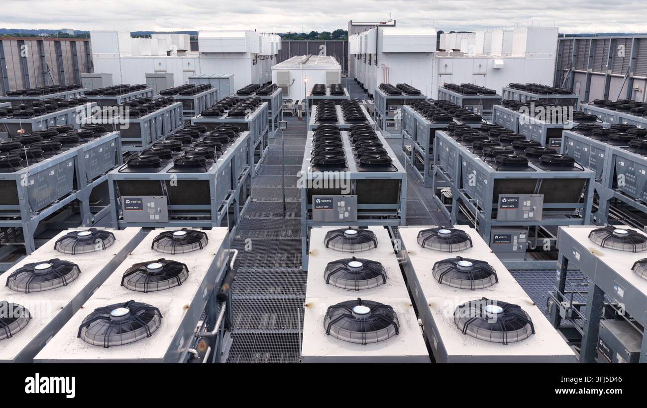 File di unità di raffreddamento grigie e ventilatori industriali si estendono sul tetto di un data center a Clifton, New Jersey, stretti passaggi metallici separano l'attrezzatura densa sottostante Foto Stock