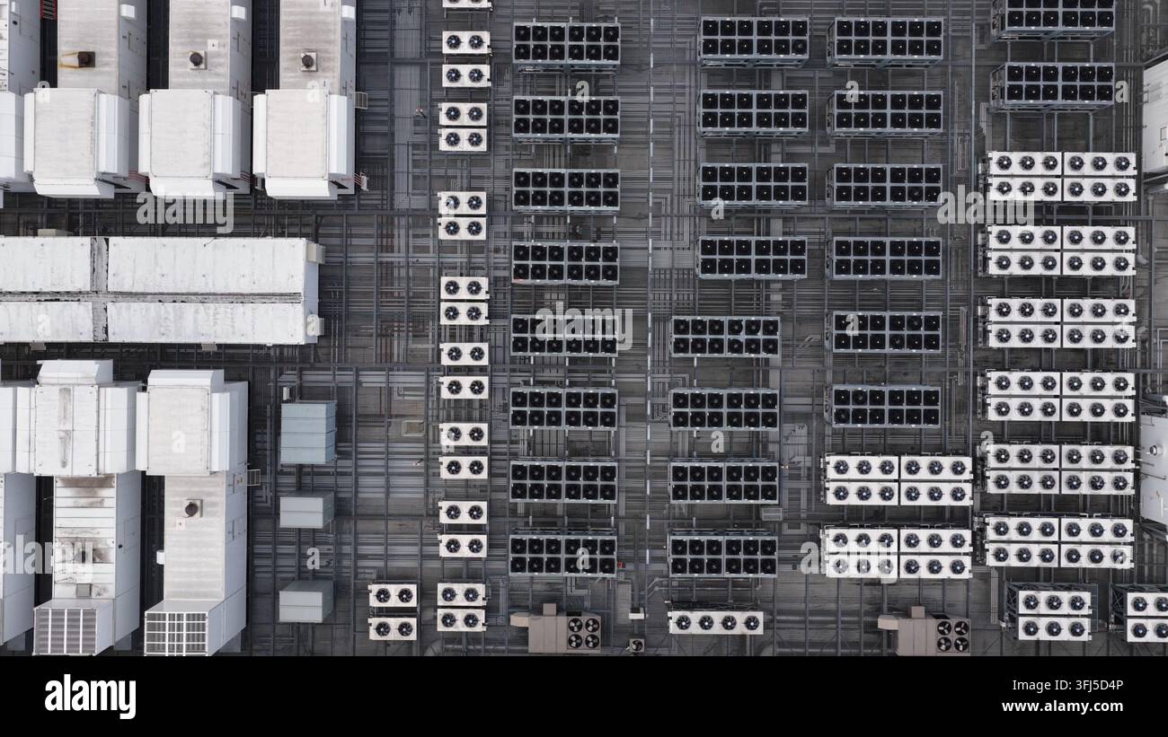 File dense di unità di raffreddamento bianche e pannelli solari coprono il tetto di un data center americano, stretti passaggi a griglia metallica separano l'attrezzatura in aree precise Foto Stock