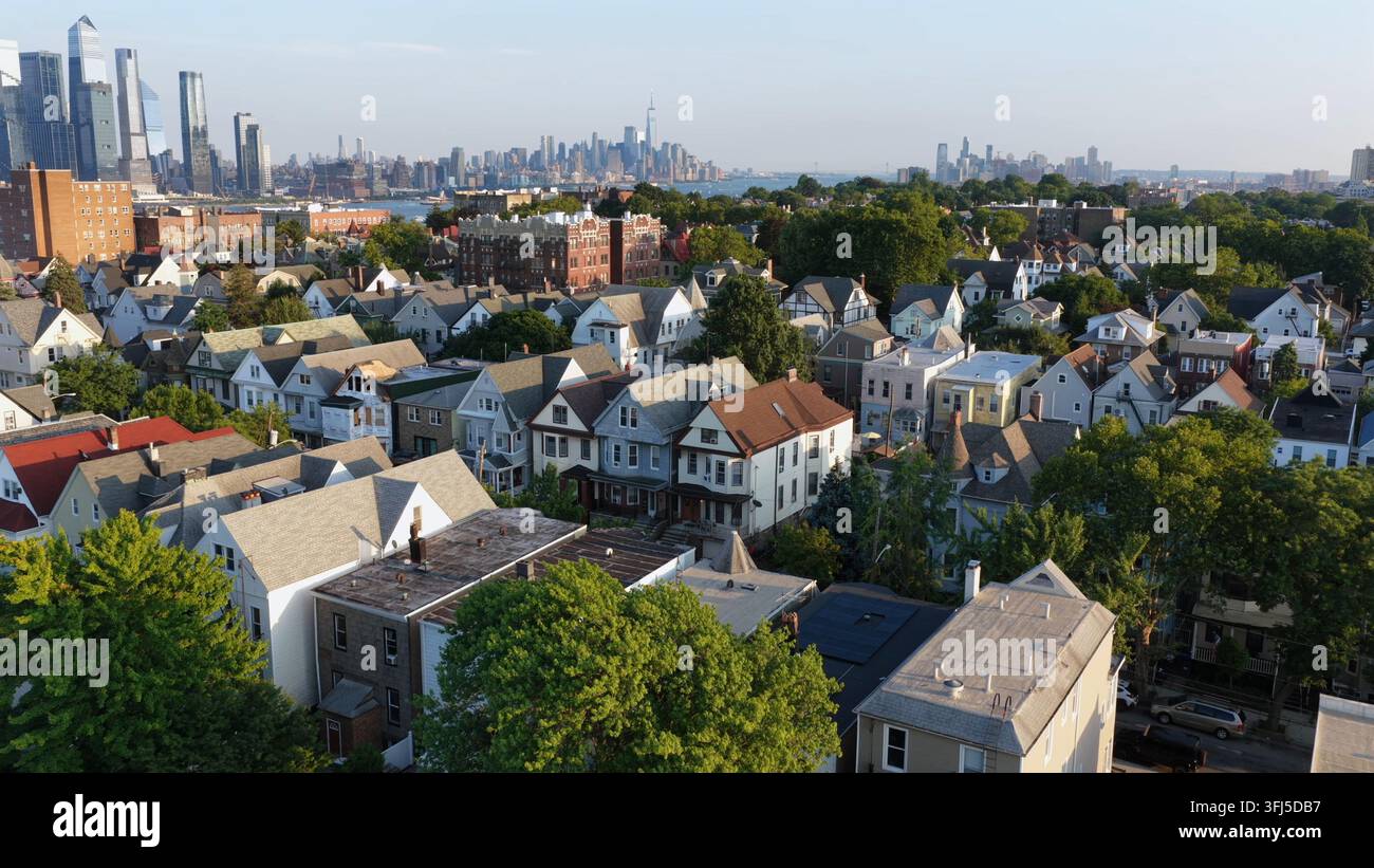 Case con tetti appuntiti e la chioma degli alberi riempiono il quartiere collinare di Union City, nel New Jersey, lo skyline di Manhattan si staglia oltre il fiume dietro le torri del lungomare Foto Stock